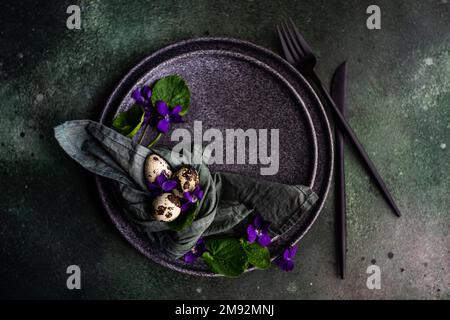 Frühlingstisch mit wilder blauer Veilchenblume auf schwarzem Teller Stockfoto