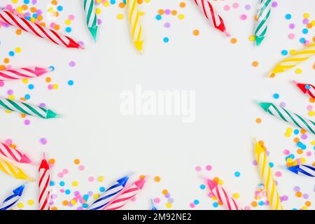 Bunte Geburtstagskuchen-Kerzen mit Süßigkeiten-Streusel. Ansichtsrahmen von oben nach unten auf weißem Hintergrund. Speicherplatz kopieren. Stockfoto