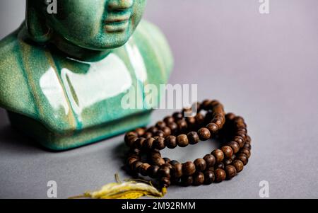 Eine Buddha-Statue und hölzerne Mala-Gebetsperlen, isoliert auf violettem Hintergrund Stockfoto