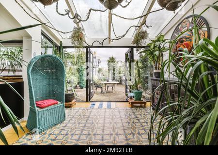 Inneneinrichtung der geräumigen Terrasse des Luxushauses mit Glasdecke und orientalischen Dekorationen in der Nähe offener Türen zum Garten im Garten Stockfoto