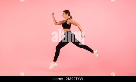 Motivierte Sporty Young Woman, Die Im Mittleren Air Über Pinkfarbenen Hintergrund Läuft Stockfoto