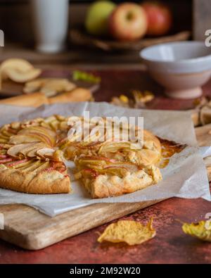 Von oben köstlicher hausgemachter Shortcrust Pie auf Holzbrett neben Herbstblättern und Äpfeln Stockfoto