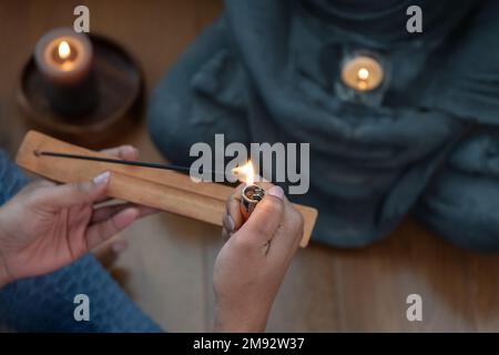 Von oben auf dem Weihrauchstäbchen mit Rauch in der Nähe brennender Kerzen und Buddha-Statue während des spirituellen Prozesses Stockfoto