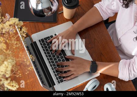 Von oben gekürzte, anonyme Freiberuflerin, die im Sessel auf dem Tisch saß, während sie ein Notebook benutzte und im Wohnzimmer an einem Projekt arbeitete Stockfoto