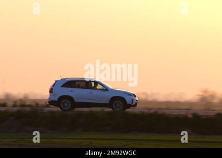 SUV-Wagen, der bei Sonnenuntergang schnell auf der Intercity-Straße fährt. Straßenverkehr am Abend Stockfoto