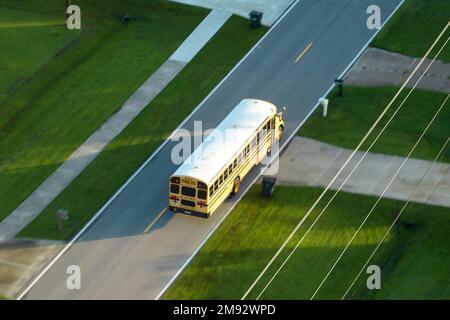 Draufsicht auf den klassischen gelben schulbus der usa, der auf der Straße der ländlichen Stadt fährt, um Kinder für ihre kleinen Kinder am frühen Morgen abzuholen. Öffentlich Stockfoto