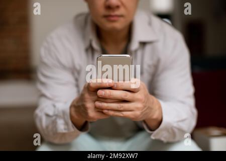 Reifer asiatischer Mann, der ein Smartphone benutzt, im Internet surft oder sich im Internet chattet, selektiver Fokus auf Handys mit dem Handy Stockfoto