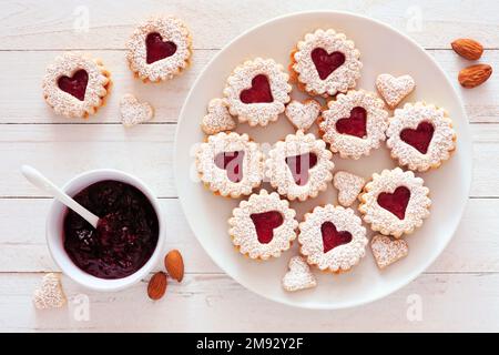 Marmelade zum Valentinstag, gefüllt mit Keksen mit Herzformen. Tischszene mit Draufsicht vor weißem Holzhintergrund. Stockfoto
