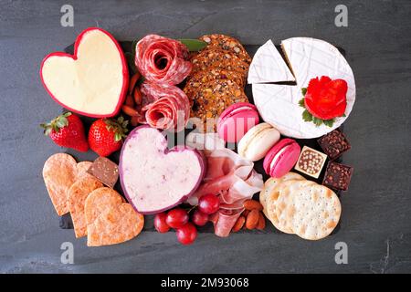 Valentinstag Wurstplatte mit verschiedenen Käsesorten, Vorspeisen und Süßigkeiten. Draufsicht auf dunklem Schieferhintergrund. Stockfoto