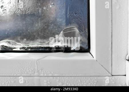 Eis bildet sich auf der Innenseite eines Fensters. Falsche Fenstermontage, Fenstereinstellung, Heizungsprobleme. Stockfoto