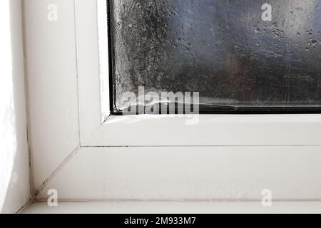 Eis bildet sich auf der Innenseite eines Fensters. Falsche Fenstermontage, Fenstereinstellung, Heizungsprobleme. Stockfoto