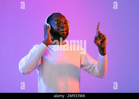 Fröhlicher schwarzer Mann mit Sonnenbrille, der Musik hört und lächelt Stockfoto