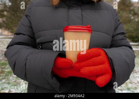 Im Winter. Kaltes Wetter. Stadtpark. Das Mädchen hält eine Tasse Kaffee in der Hand (Nahaufnahme). Lebensstil. Spaziergänge im Freien Stockfoto