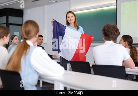 Erwachsene Lehrerin, die Schülern die französische Flagge zeigt Stockfoto