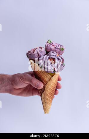 Mans Hand hält eine Waffelform mit süßen pastellfarbenen Marshmallow-Pfingstrosen auf einem hellen, isolierten Hintergrund. Modell, Raum kopieren. Kleines Geschäft, Gebäck Stockfoto