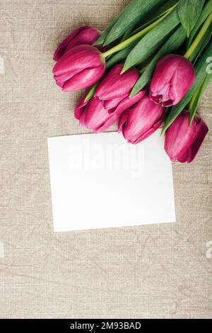 Lila Tulpen und leere Karte auf grauer Tischdecke. Frühjahrsferien-Konzept. Draufsicht, flaches Lay, Modell. Stockfoto