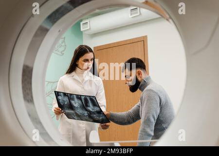 CT-Scan-Radiologe zeigt dem Patienten im Computerscanraum eine Röntgenaufnahme des Abdomens. CT-Arzt konsultiert den Patienten und zeigt dem Patienten die Thoraxröntgenaufnahme Stockfoto