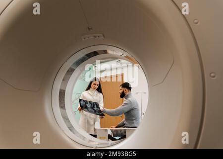 CT-Arzt, der den Patienten konsultiert und dem Patienten im Computertomographieraum das Thoraxröntgenbild zeigt. CT-Scan-Radiologe zeigt dem Patienten eine Röntgenaufnahme des Abdomens Stockfoto