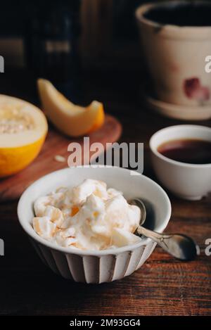 Schüssel mit hausgemachtem Eis, gemischt mit Melone und bedeckt mit Beerensirup auf einem Holztisch Stockfoto