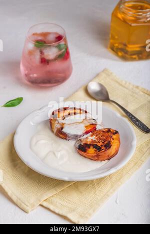 Serviert werden gegrillte Pfirsiche mit Honig und Schlagsahne auf weißem Teller und ein Glas Himbeere, Mint-Cocktail Stockfoto