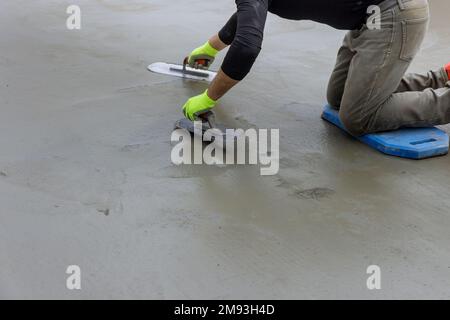 Masonry worker smoothing plastered concrete to cement floor while holding steel trowel in hand while working Stockfoto