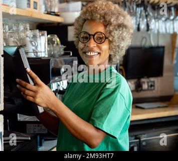 Porträt einer afroamerikanischen Kellnerin in einem Pub an der Kasse, die vor der Kamera lächelt Stockfoto