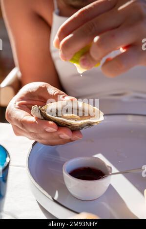 Die junge Frau in weißem Kleid isst im französischen Restaurant frische, lebende Creuze-Austern mit Zitronensaft und Meeresfrüchten Stockfoto