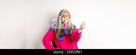 Lustige asiatische Frau starrte wütend und verwirrt, schüttelnde Finger, mürrisch vor weißem Hintergrund stehend Stockfoto