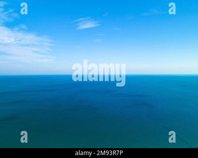 Fantastische weiße Wolken mit blauem Himmel über dem ruhigen Meer und Sonnenlicht, Luftblick auf die Wasseroberfläche des offenen Meeres, sonniger klarer Himmel und Wolken über oc Stockfoto
