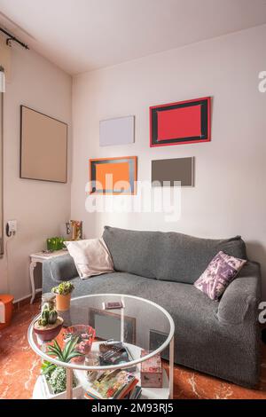 Wohnzimmer mit kleinem grauen Sofa und rundem Metall- und Glastisch auf rotem Fliesenboden Stockfoto