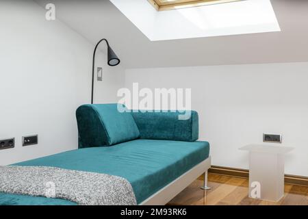 Wohnzimmer eines Ferienwohnungen im Loft-Stil mit Dachfenstern in der abfallenden Decke und langem Chaissofa aus grünem Samt mit grauem Metallrahmen Stockfoto