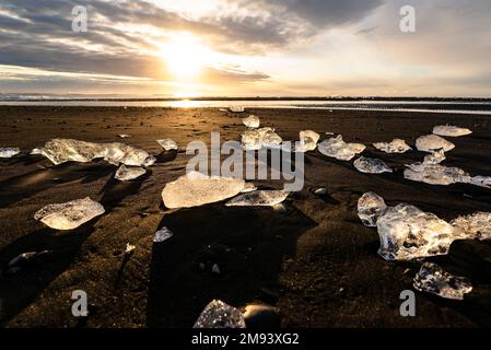 Malerische Landschaft mit hinterleuchteten Eisstücken, die auf dem schwarzen Sand von Diamond Beach, Breiðamerkursandur in der Dämmerung, Island, Vatnajökul angespült wurden Stockfoto