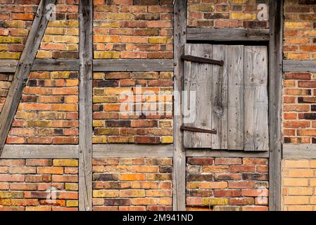 Verwitterter Holzrahmen mit gebleichten Holzbalken, roten Ziegelsteinen und einer kleinen Holztür Stockfoto