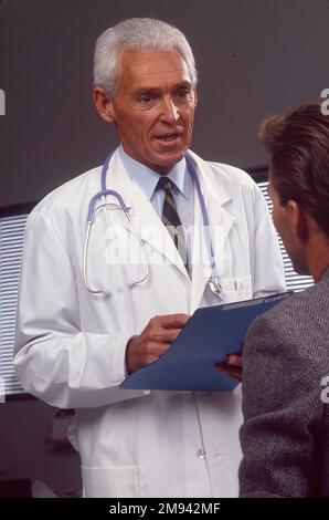 Nahaufnahme des älteren weißen männlichen Arztes über die medizinischen Aufzeichnungen mit einem männlichen Patienten gehen Stockfoto