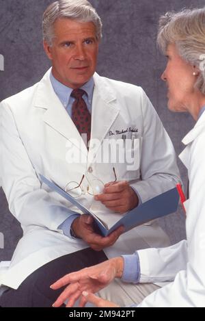 Nahaufnahme eines älteren männlichen Arztes, der ein Gespräch mit einer weiblichen Ärztin führt, die gute medizinische Aufzeichnungen hat Stockfoto