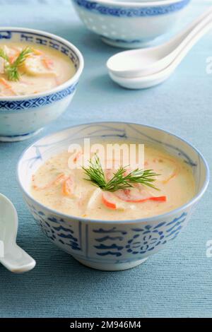 Scharfe thailändische Hühnersuppe in orientalischen Schüsseln auf blauem Hintergrund in vertikaler Form. Wärmende Kost für die Wintersaison. Konzentriere dich auf Dillgarnierung. Stockfoto