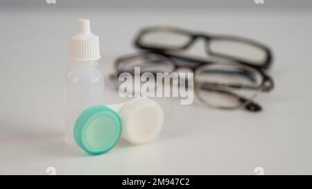 Zwei Brillengläser und Kontakttropfen in den Augen auf einem weißen Tisch. Stockfoto