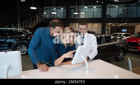 Kaukasisches Ehepaar wählt ein Auto in einem Autohaus auf digitalen Tablets. Stockfoto