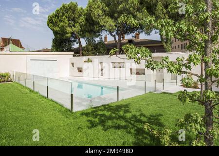 Wunderschöner Swimmingpool eines luxuriösen Einzelhauses mit Marmorfliesen und einer Wand mit Nischen für Außenpflanzen, Glaszaun mit Metallstil Stockfoto