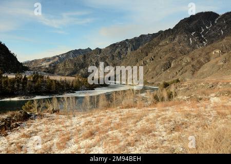 Blick von der Spitze des Hügels am geschmolzenen, gewundenen Bett eines wunderschönen Flusses, der in einem sonnigen Winter durch ein schneebedecktes Tal in den Bergen fließt Stockfoto