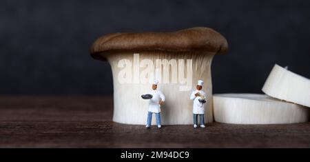 King Austernpilze und zwei Miniaturköche. Ein Konzept über Miniaturmenschen und Pilzgerichte. Stockfoto