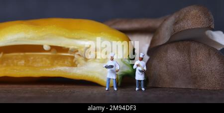 Zwei Miniaturköche mit gelben Paprika und King Oyster Pilzen. Das Konzept des Miniaturmenschen und frischer Zutaten. Stockfoto