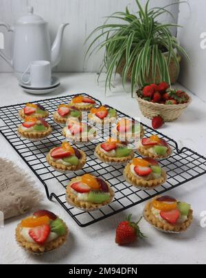 Mini-Obstkuchen garniert mit ​​kiwi-Scheiben, ​​orange-Scheiben, ​​grapes-Scheiben und ​​strawberries-Scheiben, serviert auf einem eisernen Tablett Stockfoto
