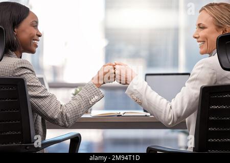 Gemeinsam ein Imperium aufbauen. Zwei Geschäftsfrauen stoßen sich die Faust an. Stockfoto