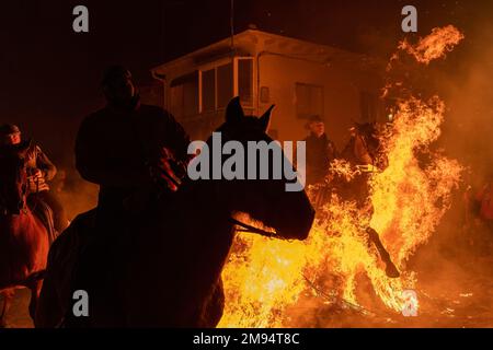 San Bartolome De Pinares, Spanien. 16. Januar 2023. Eine Reitgruppe reitet durch ein Lagerfeuer mit Pinienzweigen im Dorf San Bartolome de Pinares während des traditionellen religiösen Festivals „Las Luminarias“ zu Ehren von San Antonio Abad (Heiliger Anthony), schutzpatron der Tiere, das jede Nacht im Januar 16 gefeiert wird. Die Reiter nehmen an einer Prozession mit ihren Pferden und Eseln Teil und überqueren die zahlreichen Lagerfeuer, die in den Straßen der Stadt angezündet werden. Kredit: SOPA Images Limited/Alamy Live News Stockfoto