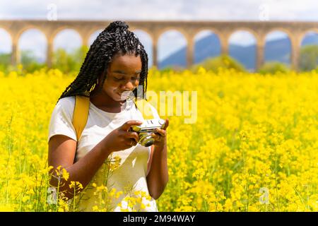 Ich schaue mir die Fotos auf einer Oldtimer-Kamera an, ein schwarzes ethnisches Mädchen mit Zöpfen, ein Reisender, in einem Feld gelber Blumen Stockfoto