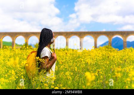 Genießen Sie den Frühling, schwarzes ethnisches Mädchen mit Zöpfen, Reisende, auf einem Feld gelber Blumen Stockfoto