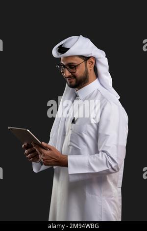 Arabischer Katar-Mann, der Tisch benutzt und auf isoliertem Hintergrund posiert. Männliches Modell in arabisch-katarischem Kleid auf isoliertem Hintergrund. Verschiedene Posen Stockfoto