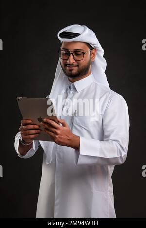 Arabischer Katar-Mann, der Tisch benutzt und auf isoliertem Hintergrund posiert. Männliches Modell in arabisch-katarischem Kleid auf isoliertem Hintergrund. Verschiedene Posen Stockfoto