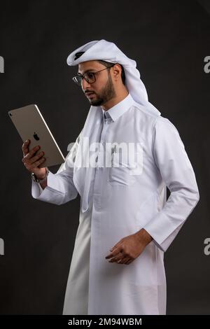 Arabischer Katar-Mann, der Tisch benutzt und auf isoliertem Hintergrund posiert. Männliches Modell in arabisch-katarischem Kleid auf isoliertem Hintergrund. Verschiedene Posen Stockfoto